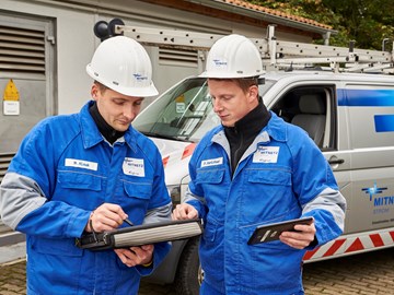 Zwei Techniker in Blaumännern betrachten Tablets vor einem Technikfahrzeug Zwei Techniker in Blaumännern betrachten Tablets vor einem Technikfahrzeug