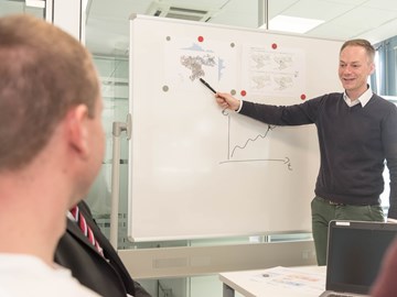 Mann deutet in einem Konferenzraum mit Kugelschreiber auf ein Präsentations-Chart Mann deutet in einem Konferenzraum mit Kugelschreiber auf ein Präsentations-Chart