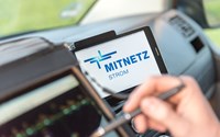 Portables Eingabegerät und Smartphone, auf dem das MITNETZ STROM-Logo zu sehen ist, im Innern eines Fahrzeugs Portables Eingabegerät und Smartphone, auf dem das MITNETZ STROM-Logo zu sehen ist, im Innern eines Fahrzeugs