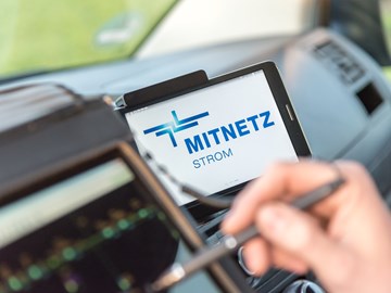Portables Eingabegerät und Smartphone, auf dem das MITNETZ STROM-Logo zu sehen ist, im Innern eines Fahrzeugs Portables Eingabegerät und Smartphone, auf dem das MITNETZ STROM-Logo zu sehen ist, im Innern eines Fahrzeugs
