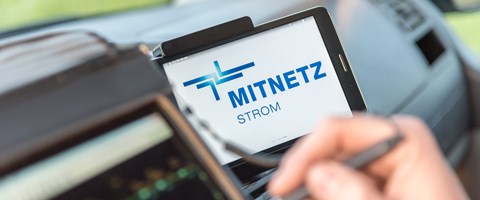 Portables Eingabegerät und Smartphone, auf dem das MITNETZ STROM-Logo zu sehen ist, im Innern eines Fahrzeugs Portables Eingabegerät und Smartphone, auf dem das MITNETZ STROM-Logo zu sehen ist, im Innern eines Fahrzeugs