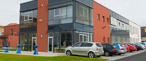 Gebäude mit Fassade in grau und orange mit Parkplätzen - Außenaufnahme  Gebäude mit Fassade in grau und orange mit Parkplätzen - Außenaufnahme
