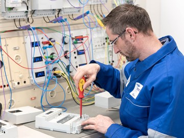 Techniker im blauen Overall arbeitet mit einem rotem Schraubenzieher an einem Gerät Techniker im blauen Overall arbeitet mit einem rotem Schraubenzieher an einem Gerät