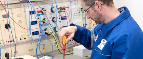 Techniker im blauen Overall arbeitet mit einem rotem Schraubenzieher an einem Gerät Techniker im blauen Overall arbeitet mit einem rotem Schraubenzieher an einem Gerät