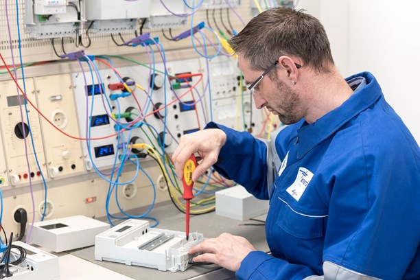 Techniker im blauen Overall arbeitet mit einem rotem Schraubenzieher an einem Gerät Techniker im blauen Overall arbeitet mit einem rotem Schraubenzieher an einem Gerät