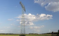 Hochspannungsmast auf einer grünen Wiese mit Windrädern unter blauem Himmel mit weißen Wolken Hochspannungsmast auf einer grünen Wiese mit Windrädern unter blauem Himmel mit weißen Wolken