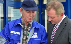 Mann im Anzug im Gespräch mit einem Mitarbeiter im Blaumann vor einem Gebäude Mann im Anzug im Gespräch mit einem Mitarbeiter im Blaumann vor einem Gebäude