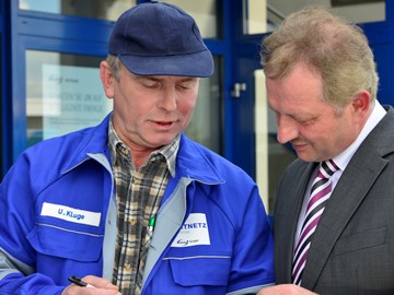 Mann im Anzug im Gespräch mit einem Mitarbeiter im Blaumann vor einem Gebäude Mann im Anzug im Gespräch mit einem Mitarbeiter im Blaumann vor einem Gebäude