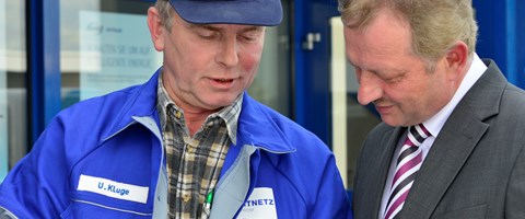 Mann im Anzug im Gespräch mit einem Mitarbeiter im Blaumann vor einem Gebäude Mann im Anzug im Gespräch mit einem Mitarbeiter im Blaumann vor einem Gebäude