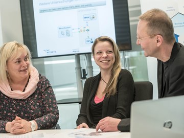 Ein Mann und zwei Frauen, an einem Tisch im Konferenzraum sitzend, im Gespräch Ein Mann und zwei Frauen, an einem Tisch im Konferenzraum sitzend, im Gespräch