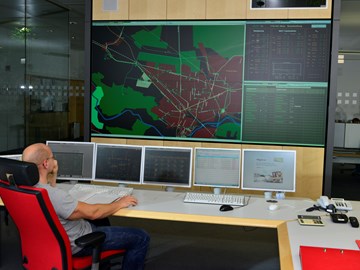 Mitarbeiter auf einem roten Stuhl vor Monitoren der Schaltleitung Mitarbeiter auf einem roten Stuhl vor Monitoren der Schaltleitung