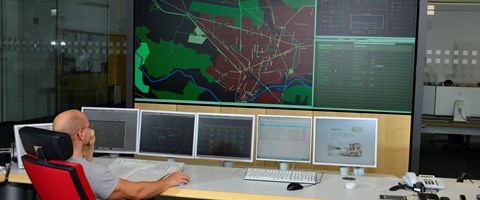 Mitarbeiter auf einem roten Stuhl vor Monitoren der Schaltleitung Mitarbeiter auf einem roten Stuhl vor Monitoren der Schaltleitung