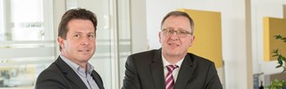 Dr. Schweer und Herr Hiersig an einem Counter über Unterlagen - blicken in die Kamera Dr. Schweer und Herr Hiersig an einem Counter über Unterlagen - blicken in die Kamera