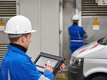 Zwei Techniker mit weißen Helmen und portablem Eingabegerät vor einer Anlage Zwei Techniker mit weißen Helmen und portablem Eingabegerät vor einer Anlage