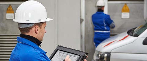 Zwei Techniker mit weißen Helmen und portablem Eingabegerät vor einer Anlage Zwei Techniker mit weißen Helmen und portablem Eingabegerät vor einer Anlage