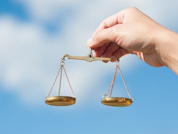 Hand hält eine goldene Waage vor einem blauen Hintergrund Hand hält eine goldene Waage vor einem blauen Hintergrund