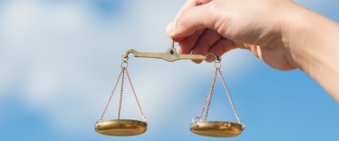 Hand hält eine goldene Waage vor einem blauen Hintergrund Hand hält eine goldene Waage vor einem blauen Hintergrund