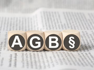 Vier Holzwürfel auf einer Zeitung zeigen die Abkürzung AGB und das Paragrafenzeichen Vier Holzwürfel auf einer Zeitung zeigen die Abkürzung AGB und das Paragrafenzeichen