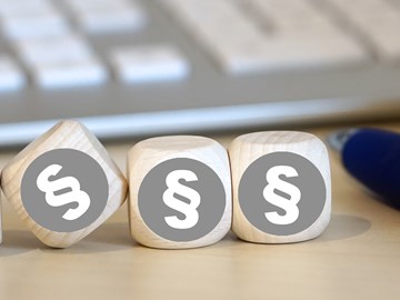 Vier Holzwürfel auf einem Schreibtisch neben einem Kugelschreiber vor einer Tastatur zeigen alle das Paragrafenzeichen Vier Holzwürfel auf einem Schreibtisch neben einem Kugelschreiber vor einer Tastatur zeigen alle das Paragrafenzeichen